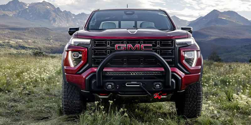 Front view of red GMC pickup truck parked in a grassy field with mountains in the background.